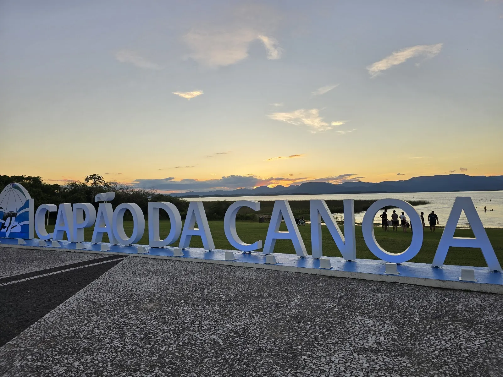 Letreiro de Capão da Canoa na beira da Lagoa dos Quadros ao pôr do sol, com a serra ao fundo